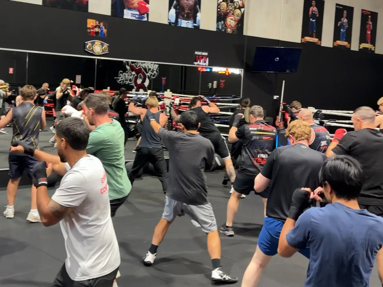 A large boxing class drilling under the fighter posters